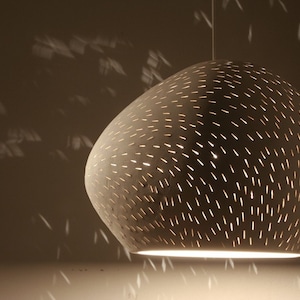 May include: A white, round, hanging light fixture with a textured surface and small holes that create a pattern of light. The light is on and casting a warm glow.