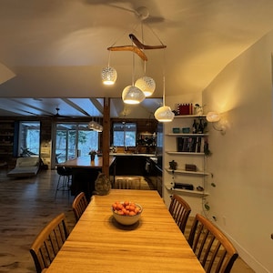 The boomerang large hangs above a clean wood dining room table in an open concept home. The visual interest of the fixture provides a focal point, and plenty of light.