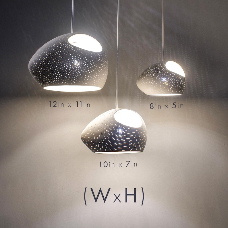 Three modern ceramic handmade pendant lights with unglazed white clay finish hanging side by side in front of a blank white wall