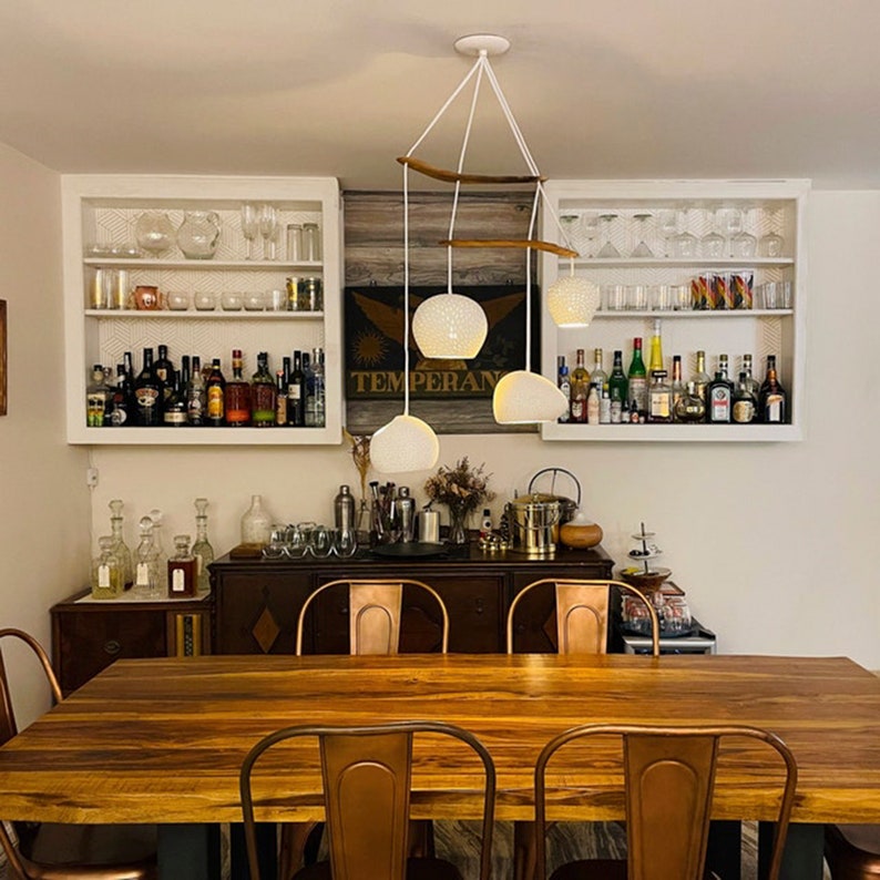 The boomerang large hangs above a wooden table, surrounded by copper bar chairs. An antique wooden buffet and white shelving dominate the background. The chandelier ties it all together with it's gentle curves and white and wood materials.