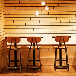 A Boomerang 3 hangs above  three cafe tables with wood and metal bar stools. Creamy elongated subway tile covers the walls.