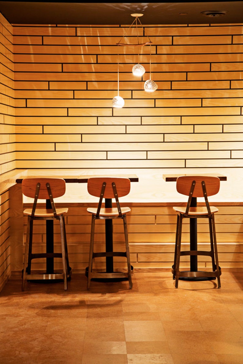 A Boomerang 3 hangs above  three cafe tables with wood and metal bar stools. Creamy elongated subway tile covers the walls.