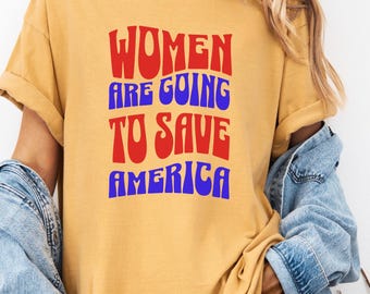 May include: Mustard yellow t-shirt with the text "WOMEN ARE GOING TO SAVE AMERICA" in red and blue. The shirt is worn with a denim jacket.