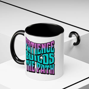 May include: White ceramic mug with a black interior and handle. The mug features the text "PATIENCE BUILDS THE PATH" in a retro, colorful font. The text is in shades of purple, teal, and blue.