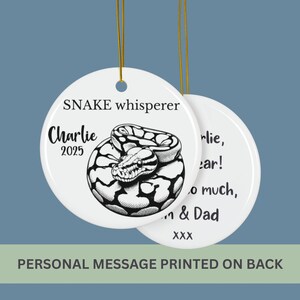 May include: White ceramic ornament with a black and white snake illustration. The ornament says "SNAKE whisperer" and "Charlie 2025". The back of the ornament has a personal message printed on it.