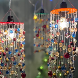 May include: Three colourful beaded pendant lights with clear glass bulbs. Each light features a variety of coloured beads, including red, blue, yellow, and orange, hanging from a metal frame.