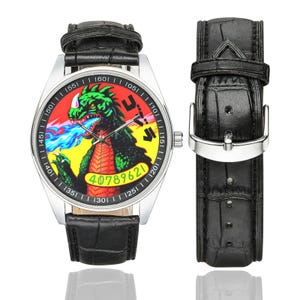 May include: A wristwatch with a silver case and a black crocodile-textured leather strap. The watch face features a green monster breathing blue fire against a red and yellow background, with the text 40789621 and Japanese characters printed.