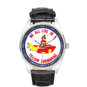May include: A silver wristwatch with a black leather strap. The watch face displays a yellow and red submarine illustration with the text "WE ALL LIVE IN A YELLOW SUBMARINE". The watch has a silver bezel and black hands.