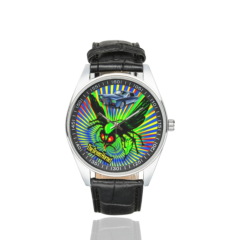 May include: A silver wristwatch with a black leather strap. The watch face displays a green hornet graphic with red eyes and a blue car against a colourful radial backdrop. The text on the watch face reads "The Green Hornet."