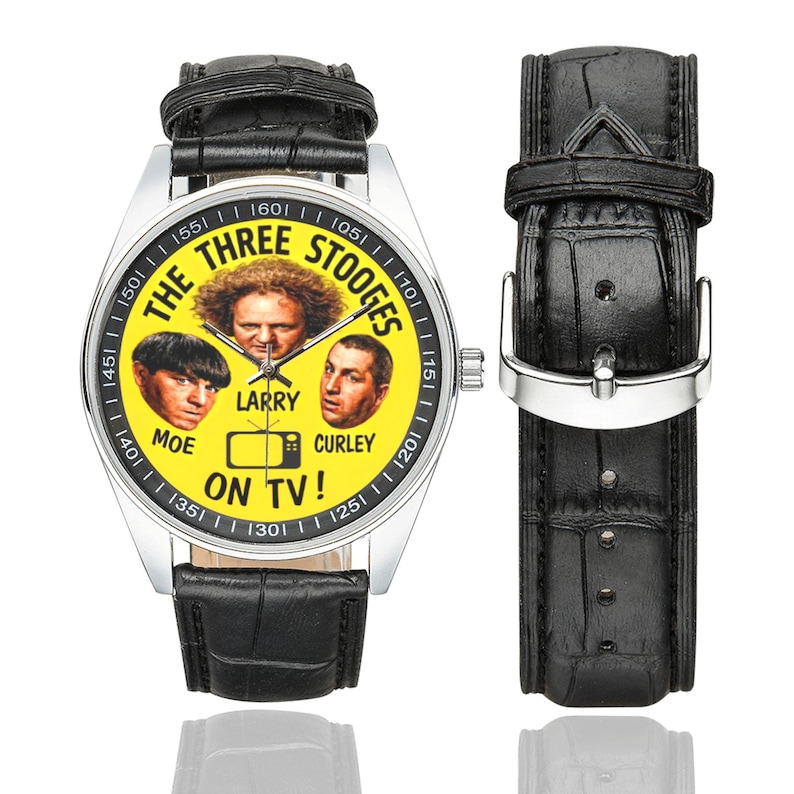 May include: A wristwatch featuring a yellow face with the text "THE THREE STOOGES" and images of Moe, Larry, and Curley. The watch has a silver case and a black leather band. The text "ON TV!" is also visible.