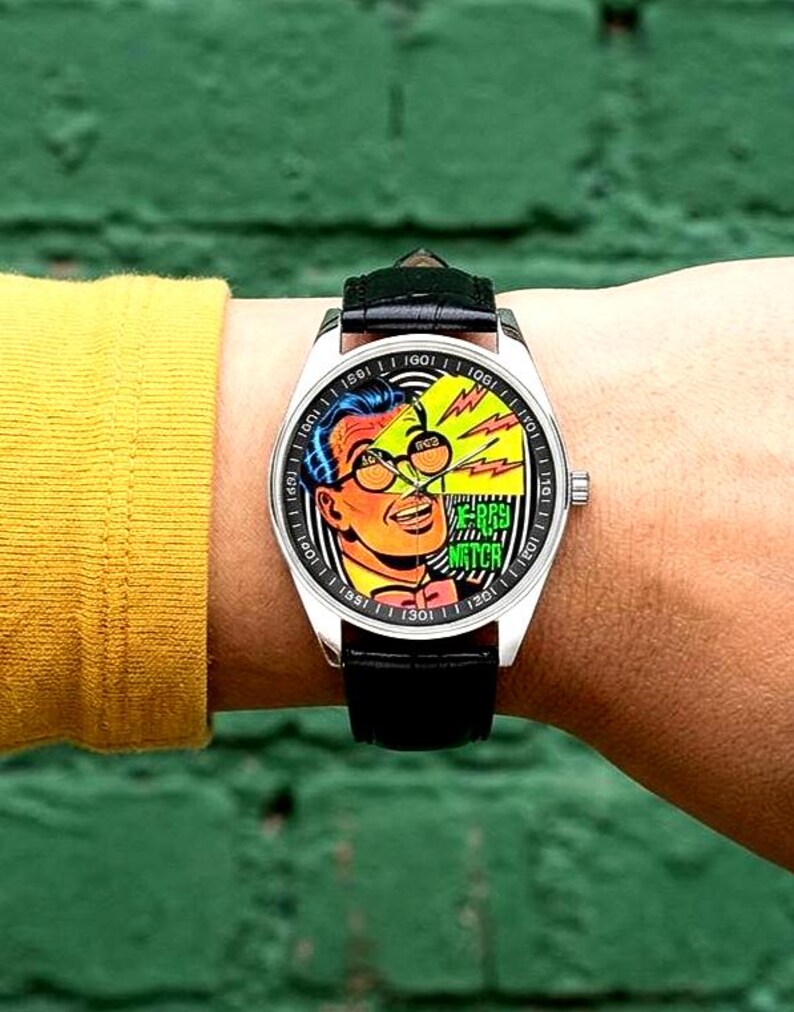 Op de afbeelding: Een polshorloge met een zwarte leren band en een zilverkleurige kast. De wijzerplaat toont een stripboekachtige illustratie van een man met een bril, met de woorden "RAY'S WATCH". Het horloge zit om een pols.