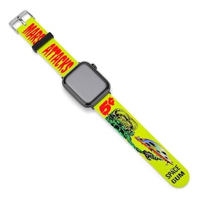 May include: A black smartwatch with a neon yellow strap. The strap features the text "MARS ATTACKS" and "SPACE GUM", along with a graphic of a green alien and a flying saucer. The strap is secured with a silver buckle.