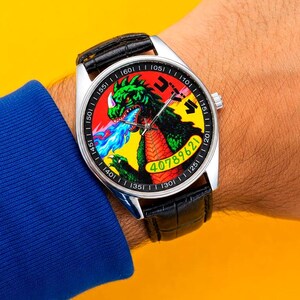 May include: A silver-tone wristwatch with a black leather strap featuring a textured pattern. The watch face displays a colorful graphic of a green monster breathing blue fire against a yellow background, with the number 40789621 and Japanese text.