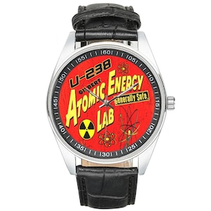 May include: A wristwatch with a silver case and a black leather band. The watch face is red with the words "U-238 Atomic Energy Lab" in yellow and white. The watch also features atomic symbols and the text "Generally Safe."