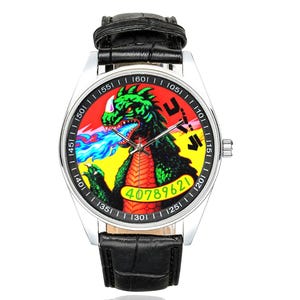 May include: A wristwatch with a black crocodile-textured leather strap and a silver-tone metal case. The watch face features a green and red monster graphic breathing blue fire, yellow background, black Japanese text, and the green number 40789621.
