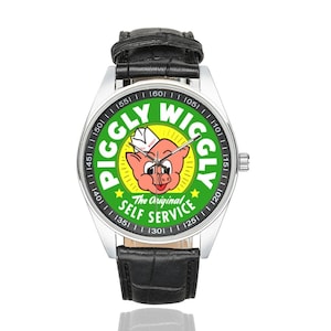May include: A wristwatch with a silver case and a black leather band. The watch face features a green background with the words "PIGGLY WIGGLY" in yellow and a cartoon pig. The text "The Original Self Service" is also visible.