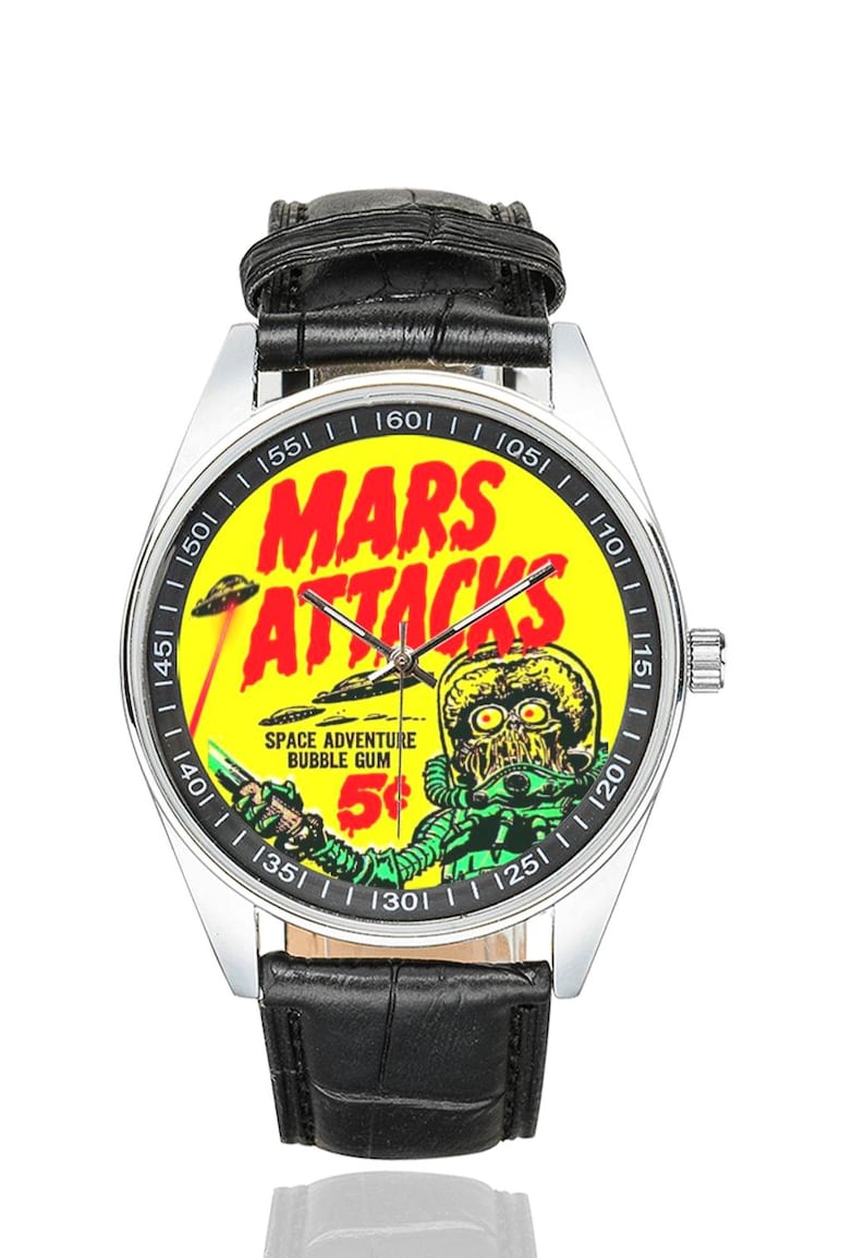 May include: A silver wristwatch with a black leather band. The watch face features a yellow background with the words "MARS ATTACKS" in red. A green alien graphic and the text "SPACE ADVENTURE BUBBLE GUM 5&cent;" are also visible.