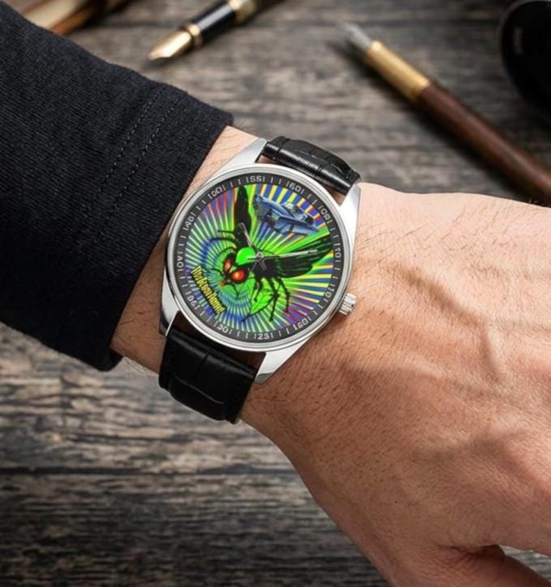 May include: A silver wristwatch with a black leather strap. The watch face displays a green and blue design with a stylized insect and the text "Work Hard, Play Harder".