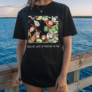 May include: Black t-shirt featuring a colorful graphic of characters from the animated film "Toy Story." The design includes Woody, Buzz Lightyear, and other characters, with the text "YOU'VE GOT A FRIEND IN ME" below the graphic.