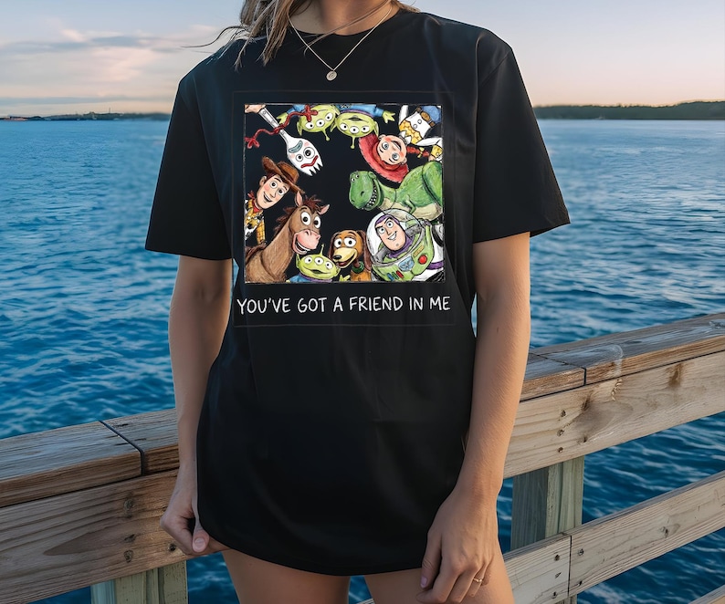 May include: Black t-shirt featuring a colorful graphic of characters from the animated film "Toy Story." The design includes Woody, Buzz Lightyear, and other characters, with the text "YOU'VE GOT A FRIEND IN ME" below the graphic.