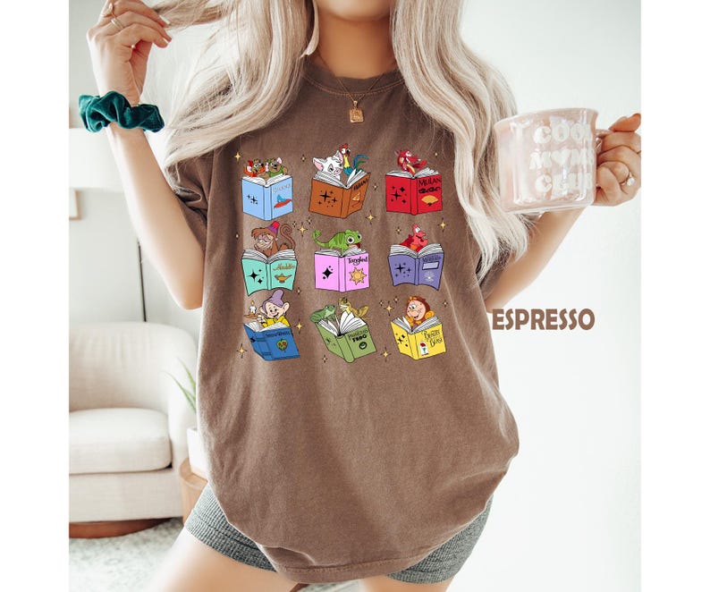 May include: Espresso-colored t-shirt featuring colorful illustrations of storybooks with various characters. The books are open, displaying images of a squirrel, frog, and other storybook characters. The word "Espresso" is printed in brown on the right side of the shirt.