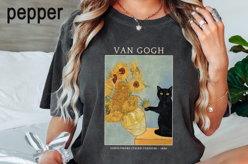 May include: Dark gray t-shirt featuring a print of Van Gogh's "Sunflowers (Third Version)" with a black cat. The text "VAN GOGH" is above the image, and "SUNFLOWERS (THIRD VERSION) - 1888" is below.