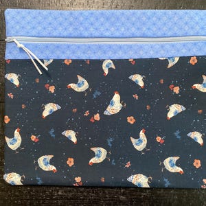 May include: A blue and white zippered pouch with a dark blue fabric featuring a repeating pattern of white chickens with blue accents. The pouch has a light blue top with a white geometric pattern.