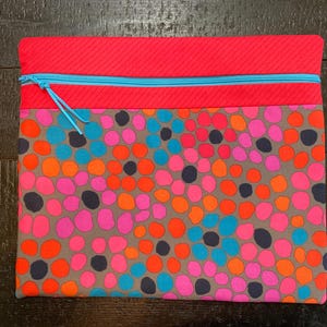 May include: A pink and gray zippered pouch with a blue zipper and a pattern of colorful dots.