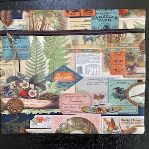 May include: A zippered pouch with a vintage floral print featuring ferns, blossoms, and a small pocket knife. The fabric also includes various text snippets, including "Lakeside Park", "Flora", "One Bait", and "Wisdom".