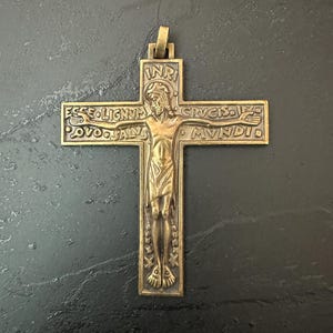 May include: A bronze-toned metal crucifix pendant featuring a central figure of Jesus. The cross is inscribed with the text INRI at the top, and the Latin phrase ECCE LIGNUM CRUCIS IN QUO SALUS MUNDI is embossed across the horizontal arms of the cross.
