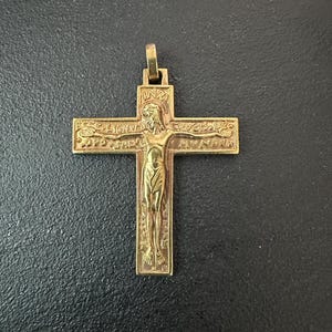 May include: A gold-toned metal crucifix pendant featuring a raised figure of Jesus on the cross. The top of the cross displays the letters INRI, while the horizontal arms are inscribed with the Latin text ECCE LIGNUM CRUCIS and SALUS MUNDI.