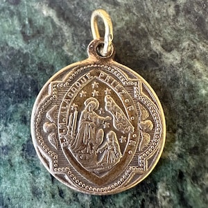 Peut inclure: Un pendentif en métal doré avec une image religieuse d'une femme tenant un enfant. Le pendentif a une boucle en haut pour l'accrocher. L'inscription sur le pendentif est "SEMPER LACOCQUE PRIEZ P.C.N."
