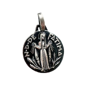 May include: A silver pendant with a black enamel background featuring an image of the Virgin Mary with the text "N-D-DE FATIMA" around the edge.