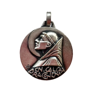 May include: Silver pendant featuring a profile of a man in a robe, with the inscription "IN. CALCA. DRAGON. IN." around the edge.