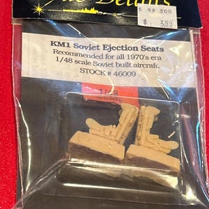 May include: A model kit of KM1 Soviet Ejection Seats, packaged in black plastic with gold text reading "True Details". The kit is for 1/48 scale Soviet aircraft from the 1970s. The ejection seats are tan in colour.