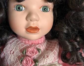 Vintage style porcelain doll features,curly dark hair,pink white lace detailing.