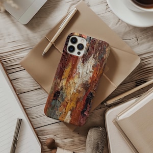 May include: A colorful phone case with a textured, abstract art design in shades of red, orange, yellow, and white. The case is lying on a brown envelope, with a pen and notebook nearby. The phone case has a camera module with three lenses.