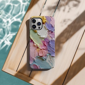 Könnte beinhalten: Smartphone-Hülle mit einem farbenfrohen abstrakten Ölgemälde-Design. Die Hülle zeigt dicke Pinselstriche in Gelb-, Weiß-, Grün-, Rosa-, Lila- und Blautönen. Die Hülle liegt auf einem Holztablett.