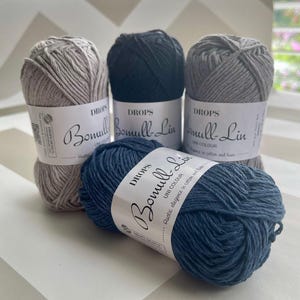 May include: Four skeins of Drops Bomull-Lin yarn in various colors: light gray, navy blue, dark gray, and a darker blue. Each skein has a white label with the yarn name and brand. The yarn is made of cotton and linen.