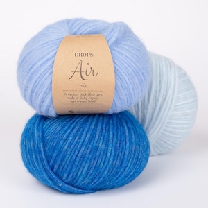May include: Three balls of Drops Air mix yarn in shades of blue. The top ball is light blue with a brown label. The label reads "DROPS Air mix" and "A medium thick blow yarn, made of Baby Alpaca and Merino Wool."