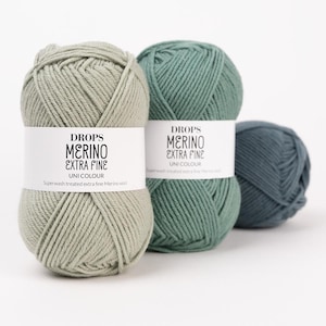 May include: Three skeins of Drops Merino Extra Fine yarn in varying shades of green. The labels read Drops Merino Extra Fine Uni Colour Superwash treated extra fine Merino wool. The yarn is arranged in a row with the lightest sage green in front.