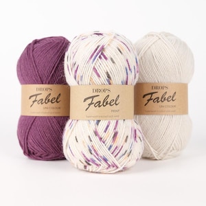 May include: Three skeins of Drops Fabel yarn in various colors. One is a solid deep purple, another is speckled with purple, blue, and orange on a cream background, and the third is a solid cream color. Each skein has a brown paper label.