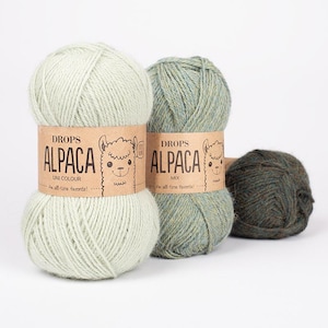 May include: Three skeins of yarn with paper labels. The first is light mint green, the second is a variegated sage green, and the third is a dark forest green. Each label features the text DROPS ALPACA, an illustration of an alpaca, and the phrase An all-time favorite!