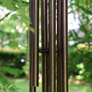 K&ouml;nnte beinhalten: Ein Set aus vertikalen, zylindrischen Windspielr&ouml;hren mit einer texturierten, bronzefarbenen und dunkelbraunen Metallic-Oberfl&auml;che. Die hohlen Metallr&ouml;hren sind parallel aufgeh&auml;ngt und werden durch ein kleines, dunkles, kreisf&ouml;rmiges Abstandselement gehalten.