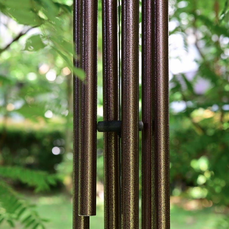K&ouml;nnte beinhalten: Ein Set aus vertikalen, zylindrischen Windspielr&ouml;hren mit einer texturierten, bronzefarbenen und dunkelbraunen Metallic-Oberfl&auml;che. Die hohlen Metallr&ouml;hren sind parallel aufgeh&auml;ngt und werden durch ein kleines, dunkles, kreisf&ouml;rmiges Abstandselement gehalten.