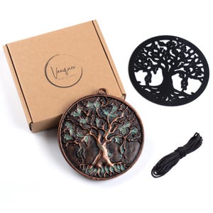 May include: A round bronze-toned metal plaque featuring a raised tree of life design with teal accents, a matching black circular metal tree cutout, a coil of black cord, and a tan cardboard box labeled with the text Vanquer Wind Chimes.