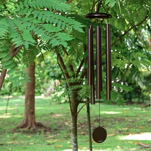 K&ouml;nnte beinhalten: Ein bronzefarbenes Windspiel mit f&uuml;nf zylindrischen Metallr&ouml;hren unterschiedlicher L&auml;nge, die an einer runden Plattform h&auml;ngen, sowie einem zentralen Kl&ouml;ppel und einem runden Windf&auml;nger an einer d&uuml;nnen schwarzen Schnur.