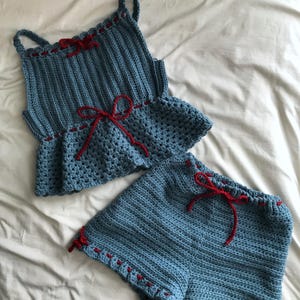 May include: A blue crocheted top and shorts set with red ribbon ties. The top has a ruffled hem and the shorts have a wide waistband.