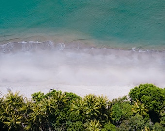 Può includere: Vista aerea di una spiaggia tropicale con sabbia bianca e acqua turchese. Alberi verdi lussureggianti costeggiano la riva.