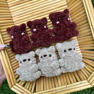 May include: Six handmade crochet teddy bears in a woven basket. Three are a deep burgundy color, and three are a light gray. Each bear has small black eyes and pink cheeks, with a cute, cuddly appearance.